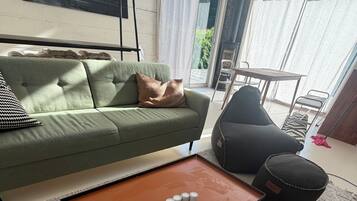 Ett modernt vardagsrum med en grön soffa, ett brunt soffbord med vita koppar och en svart pall.