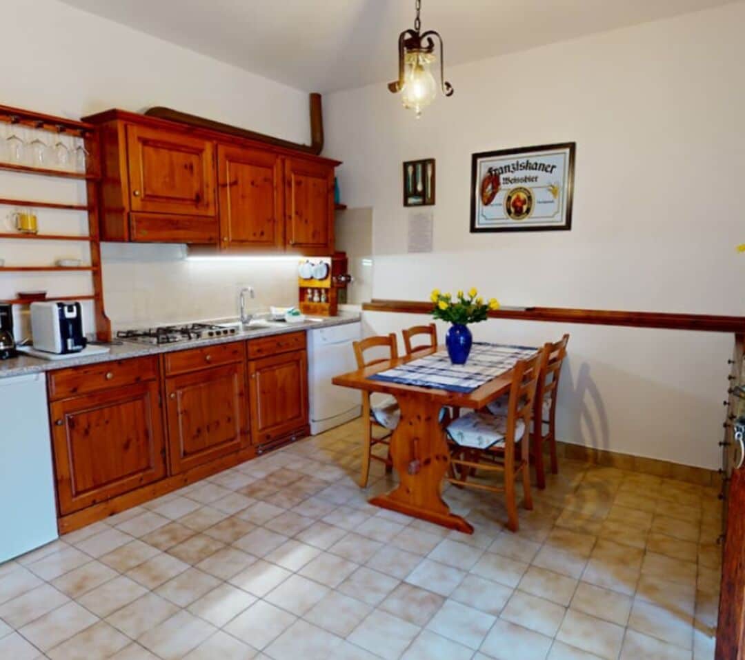 A kitchen with wooden cabinets, a dining table with chairs, and a hanging light fixture.