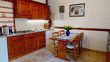 Una cocina con gabinetes de madera, una mesa de comedor con sillas y una lámpara colgante.