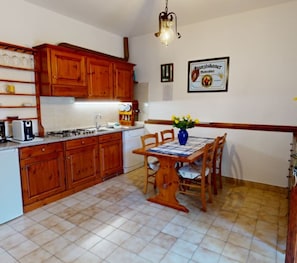 A kitchen with wooden cabinets, a dining table with chairs, and a hanging light fixture. - Toscana Vacanze (MONTAIONE)