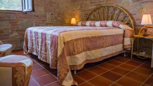 A bedroom with a brick wall, a bed with a patterned bedspread, two bedside lamps, and a chair. - Toscana Vacanze (MONTAIONE)