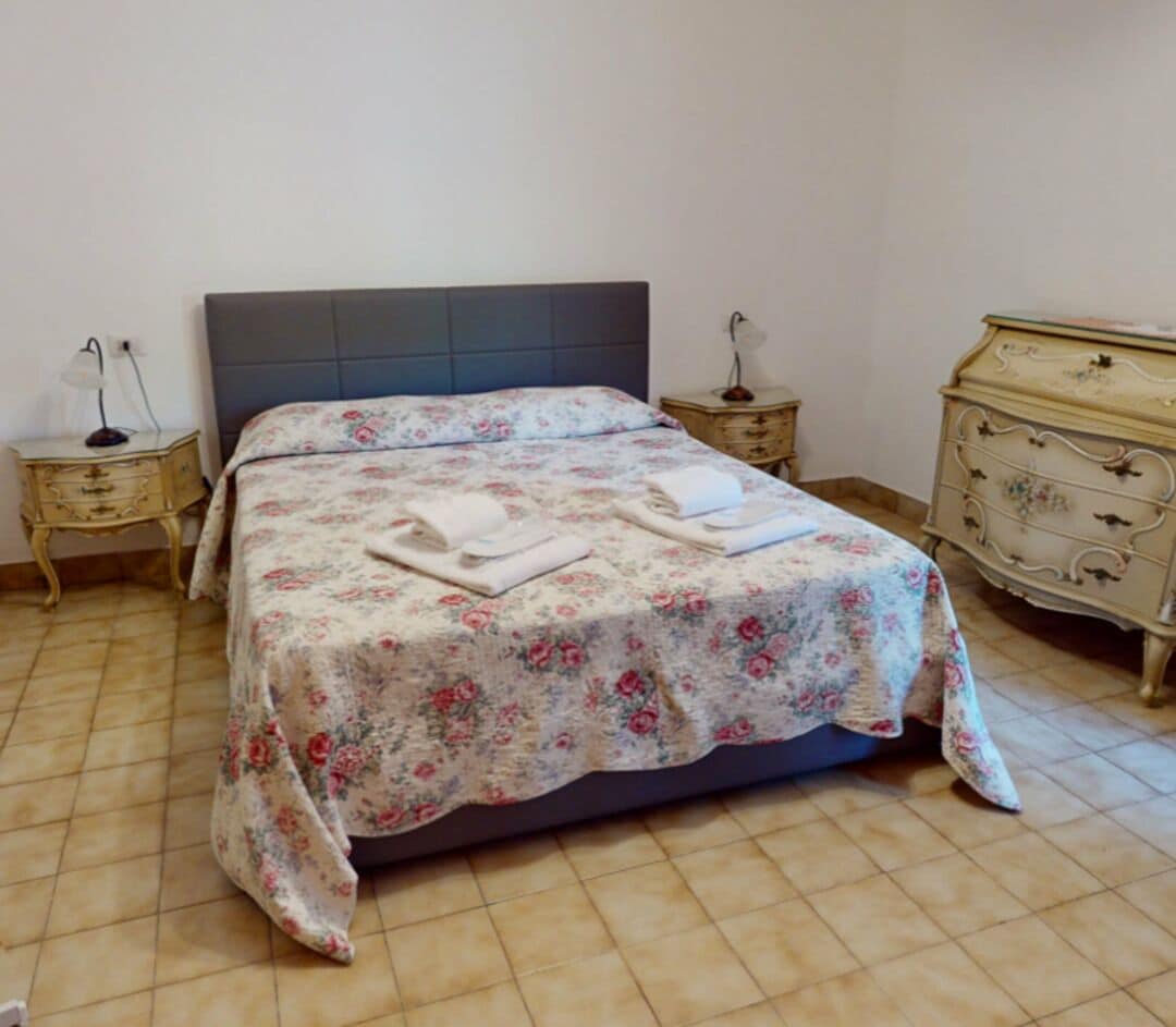 Una cama con cubrecama floral, dos mesitas de noche y un aparador.