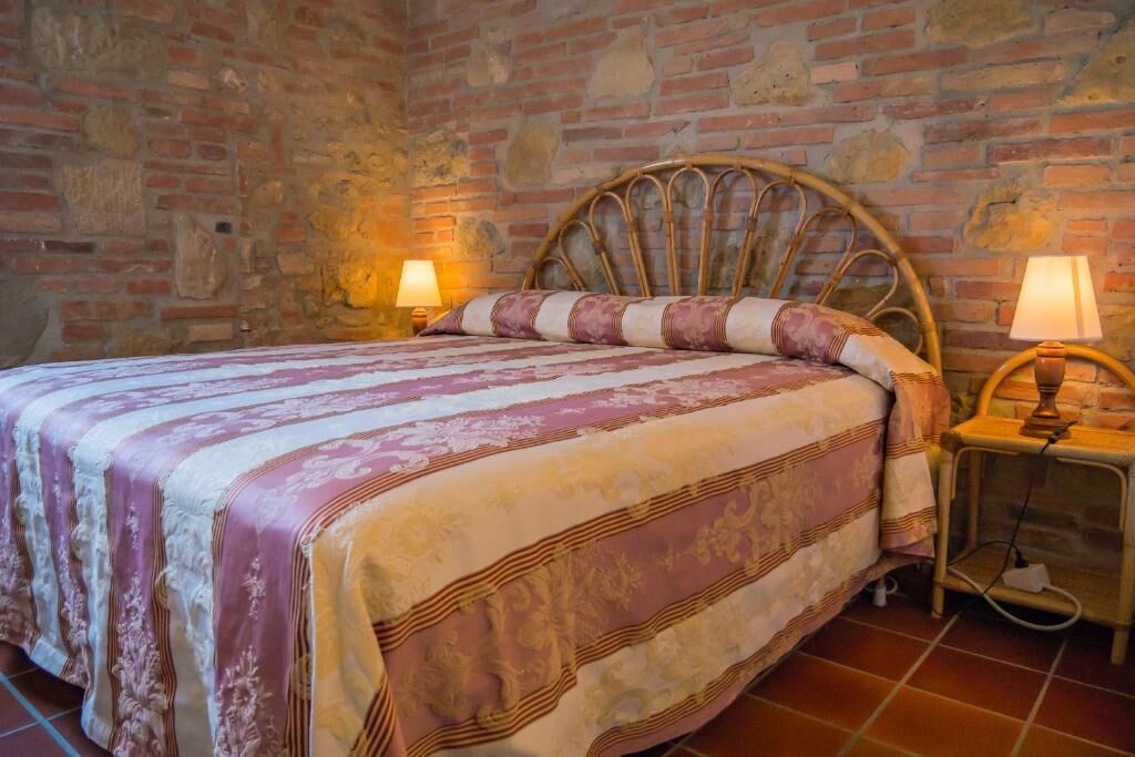 Una cama con cabecera, dos lámparas de noche y una colcha estampada en una habitación con paredes de piedra.