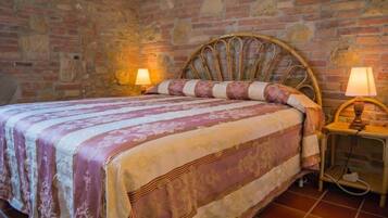 Una cama con cabecera, dos lámparas de noche y una colcha estampada en una habitación con paredes de piedra.