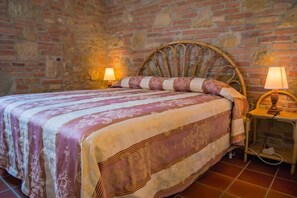 Una cama con cabecera, dos lámparas de noche y una colcha estampada en una habitación con paredes de piedra.