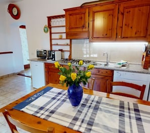 A kitchen with wooden cabinets, a microwave, a sink, and a vase with yellow flowers on a table. - Toscana Vacanze (MONTAIONE)