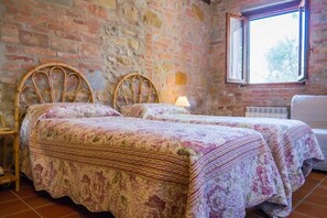 A room with two wooden beds with floral bedding, a brick wall, a window, and a radiator. - Toscana Vacanze (MONTAIONE)
