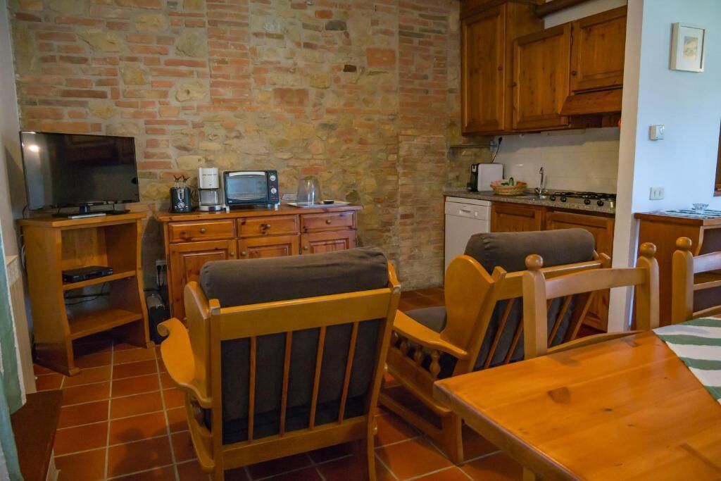 Un espacio habitable compacto con pared de piedra, mobiliario de madera, televisor, cafetera y una pequeña zona de cocina.