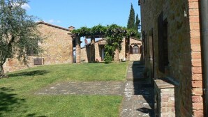 A courtyard with stone buildings, a grassy area, and a brick wall. - Toscana Vacanze (MONTAIONE)