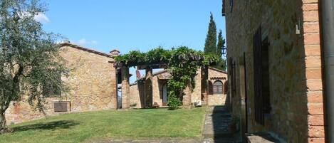 A courtyard with stone buildings, a grassy area, and a brick wall.