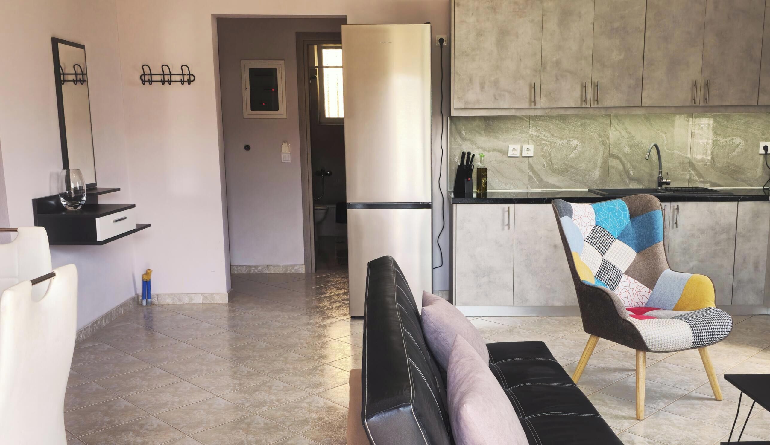 A modern living room with a sofa, a colorful armchair, and a kitchen area with cabinets and a countertop.