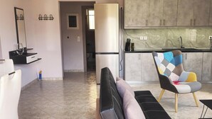 Ein modernes Wohnzimmer mit Sofa, einem farbenfrohen Sessel und einer Küchenzeile mit Schränken und Arbeitsplatte.