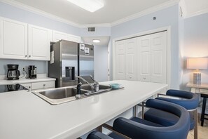 Eine moderne Küche mit einem Edelstahl-Kühlschrank, einer Spüle mit Wasserhahn und einer Bar mit blauen Stühlen.