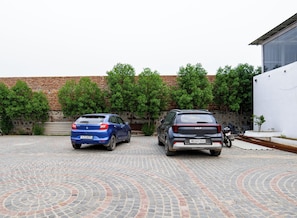 Two cars parked in a courtyard with a brick wall and greenery in the background.