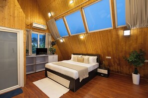 Ein Schlafzimmer mit schrägem Dach, einem Bett, einem Fernseher, einem Schreibtisch und einem Fenster.