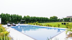A rectangular swimming pool with a clear blue edge, surrounded by a white deck. There are lounge chairs and a small table on the deck.