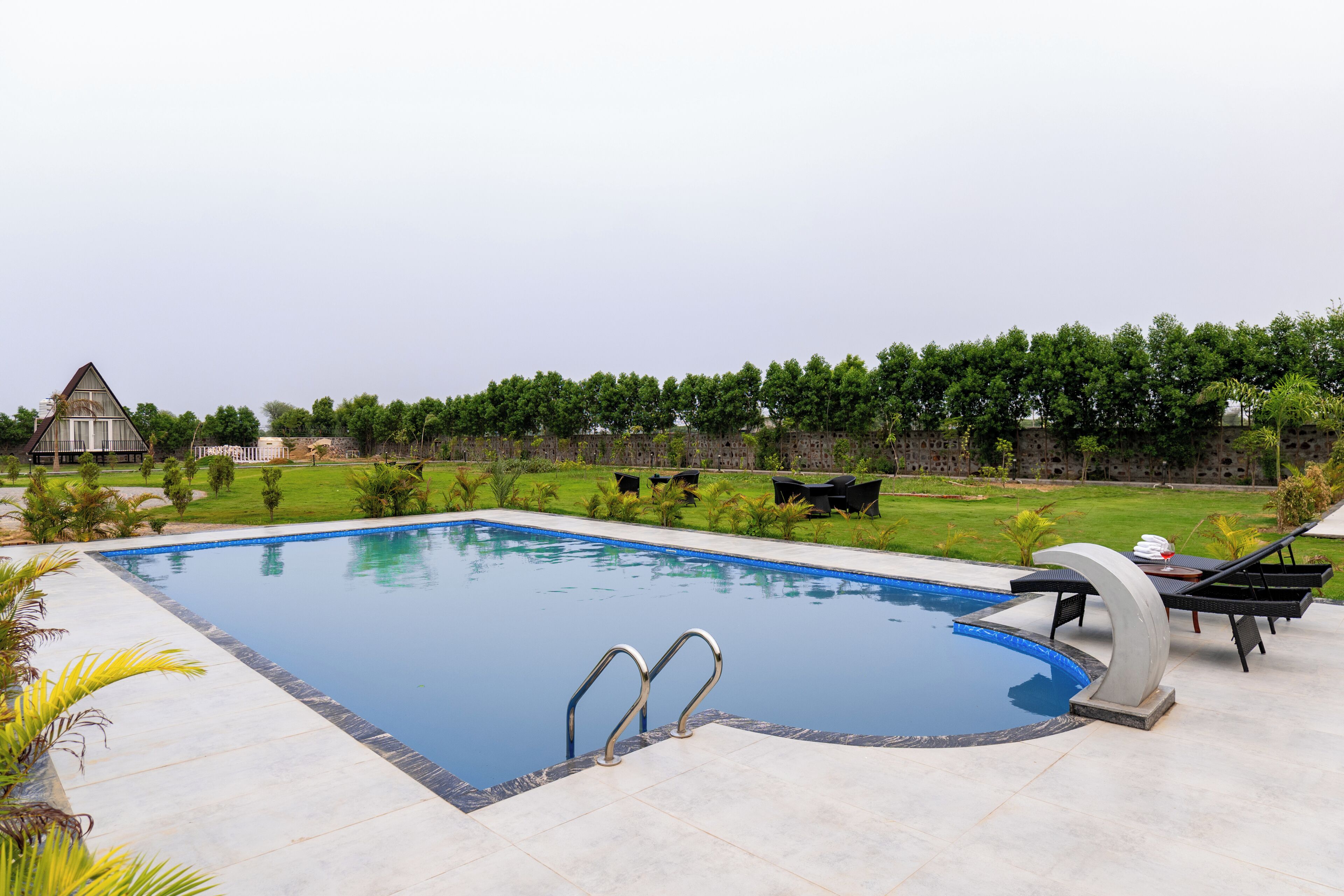 Una piscina con borde azul cristalino, rodeada de césped cuidado y un muro de piedra.