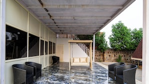 A covered outdoor area with a marble floor, wicker furniture, and a staircase leading to an upper level.