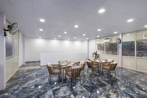 A conference room with a marble floor, wicker chairs, a whiteboard, and a view through large windows.
