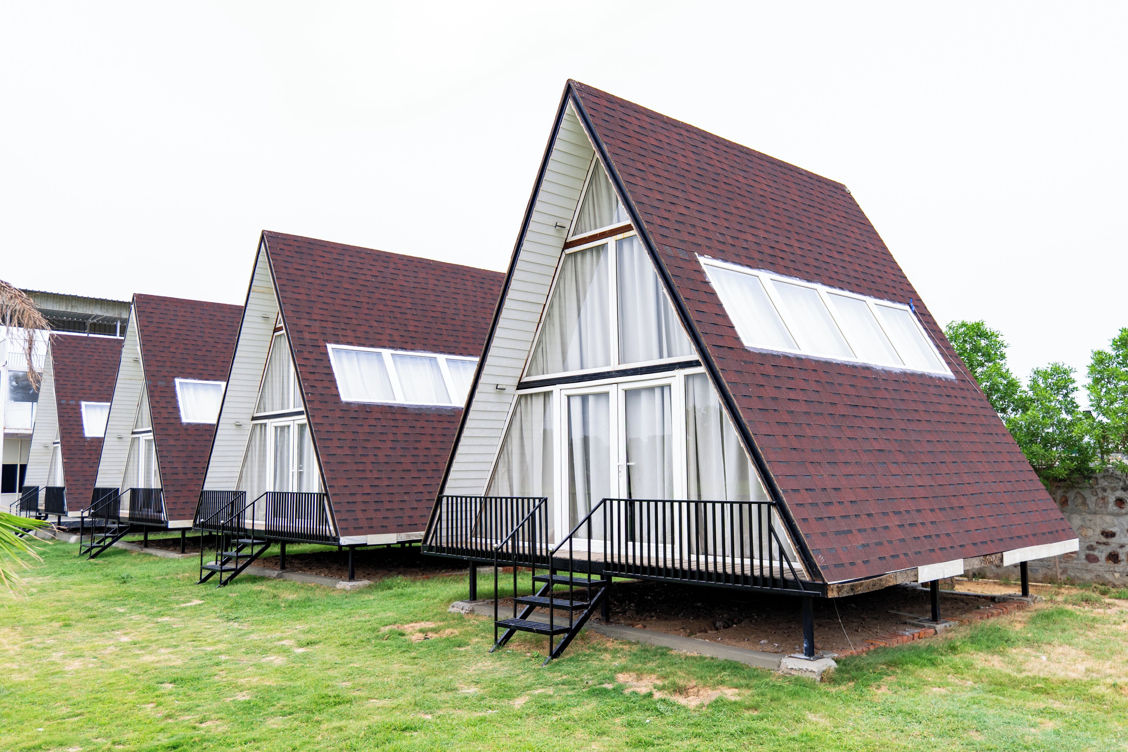 Une rangée de cabanes à toit triangulaire, dotées d’escaliers extérieurs et entourées d’une pelouse.
