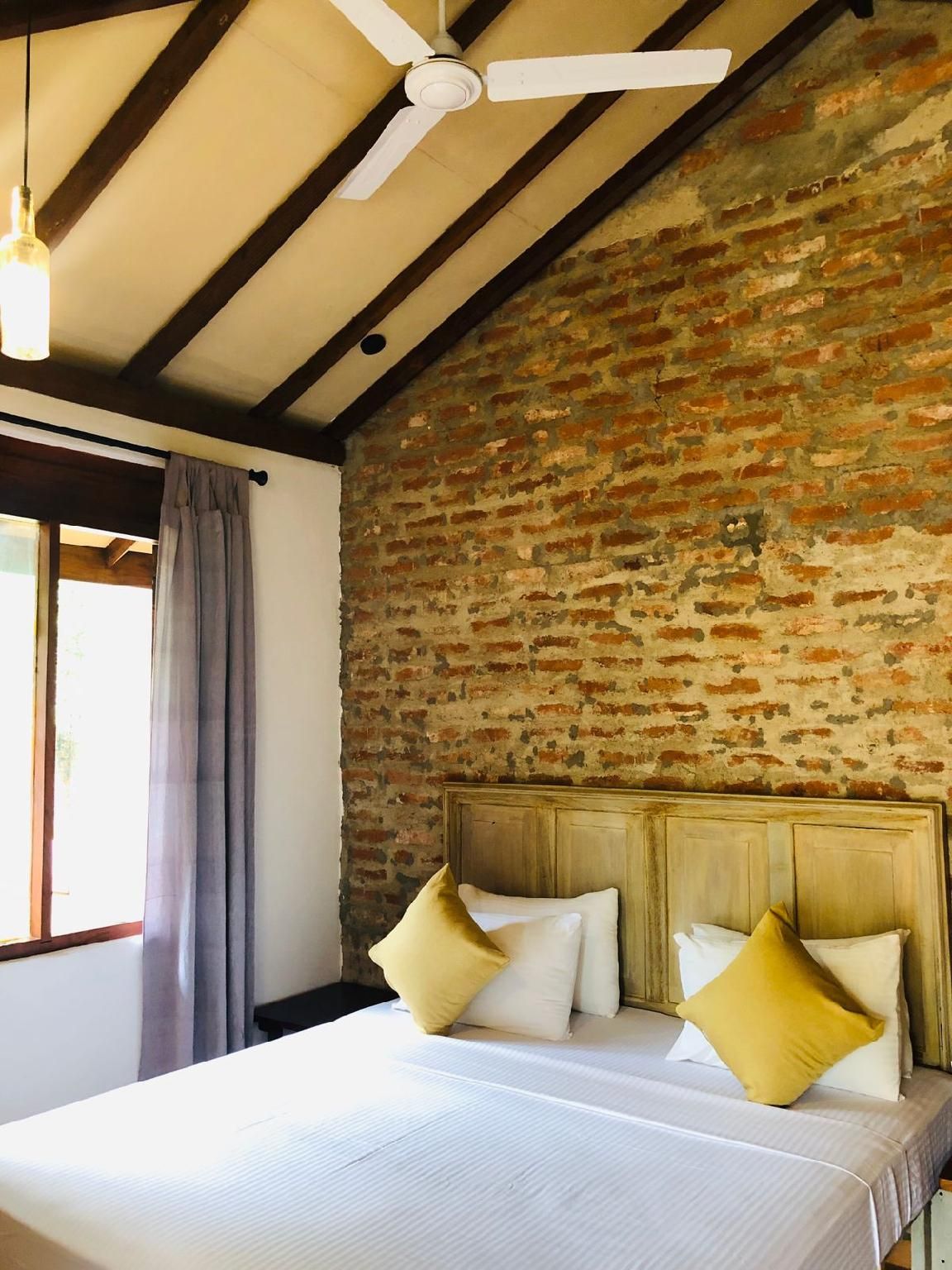 A room with a bed, a headboard, a ceiling fan, and a brick wall.