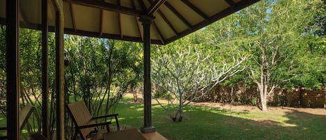 A covered patio with wooden furniture and a view of a well-maintained garden.