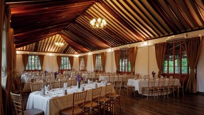 Une salle de banquet dotée de nombreuses tables rondes, d’un parquet en bois et de grandes fenêtres.