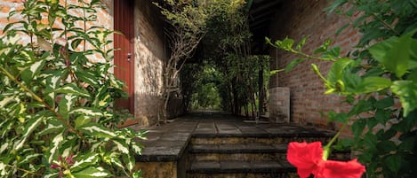 A narrow stone staircase leading to a covered area with brick walls and greenery.