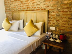 A hotel room with a bed, pillows, a bedside table with a water bottle, cups, and a red kettle.