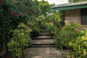 A stone staircase leading up to a building with a green roof, surrounded by lush greenery and flowering plants.