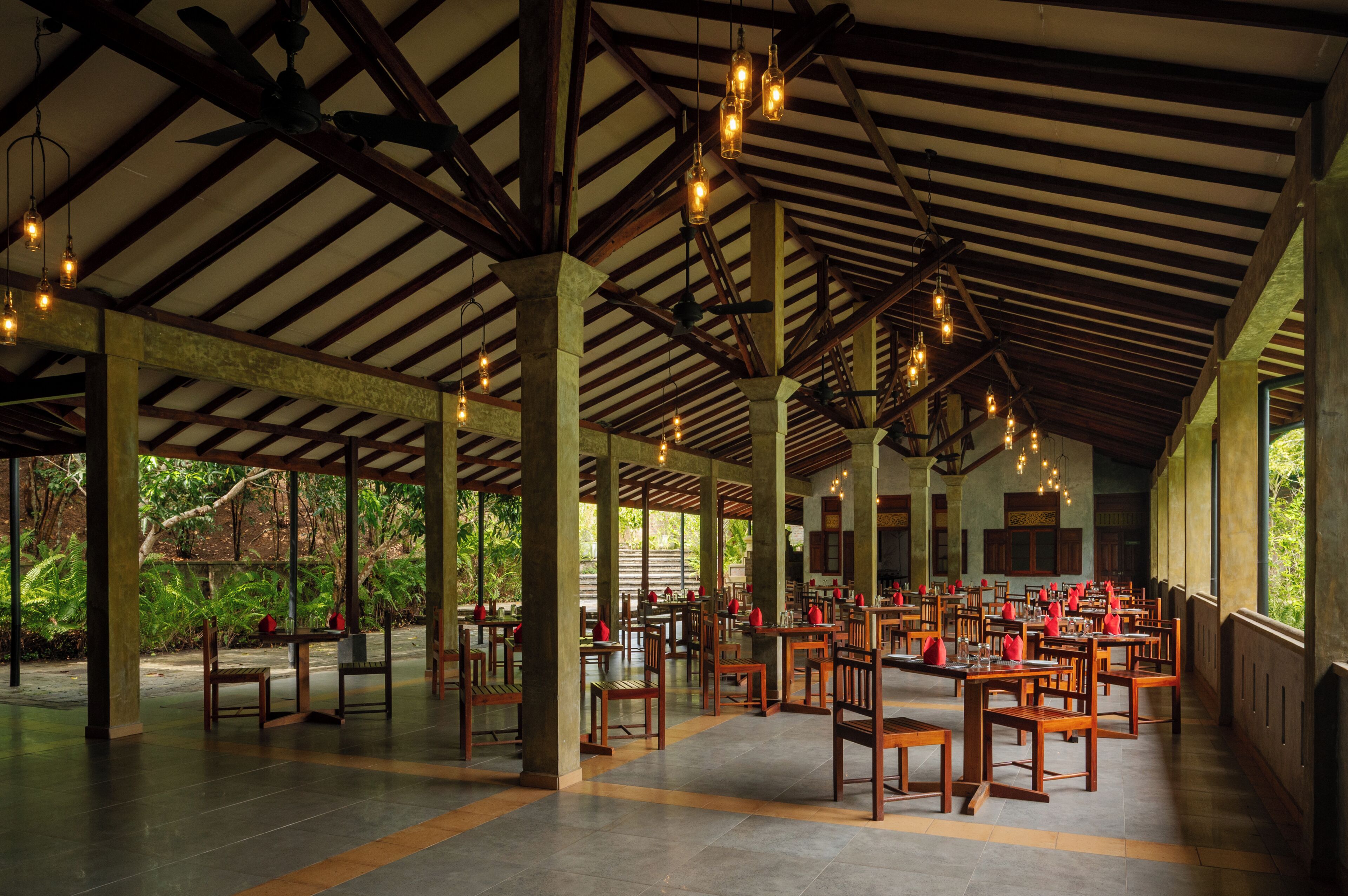 Un vaste espace couvert doté de poutres et de colonnes en bois, de tables avec des chaises et de luminaires suspendus.