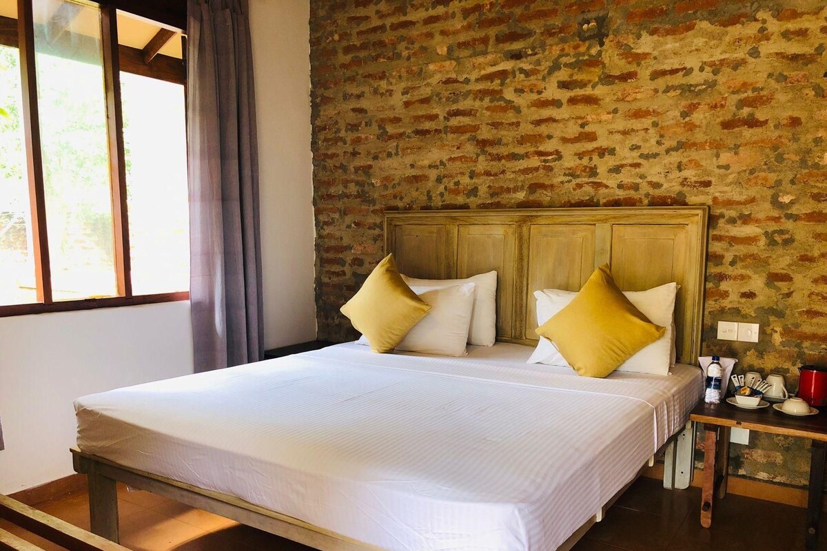 Quarto com cama grande, cabeceira de madeira e parede de tijolos.