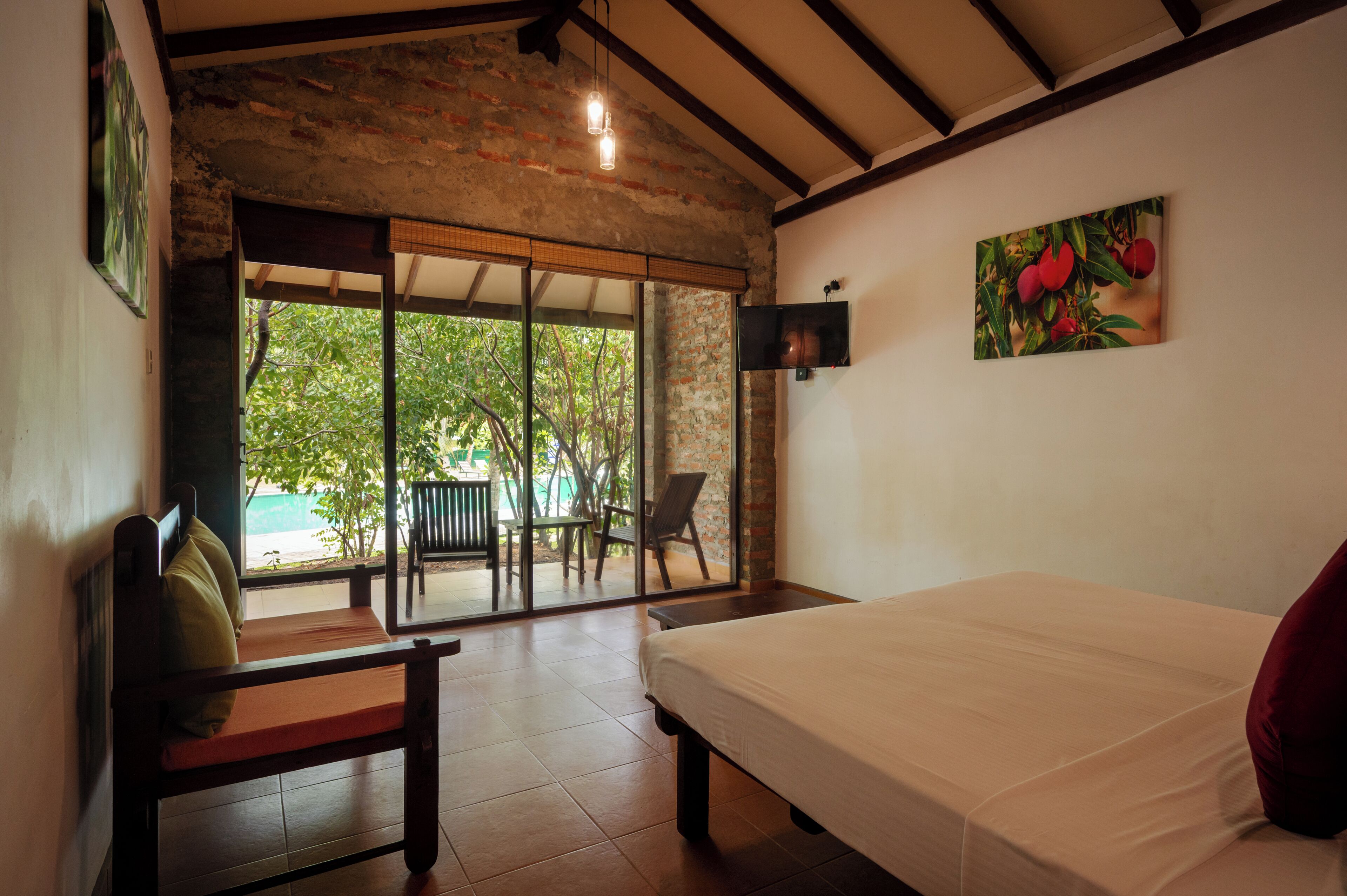 A room with a bed, a chair, a table, a TV, and a view of greenery outside.