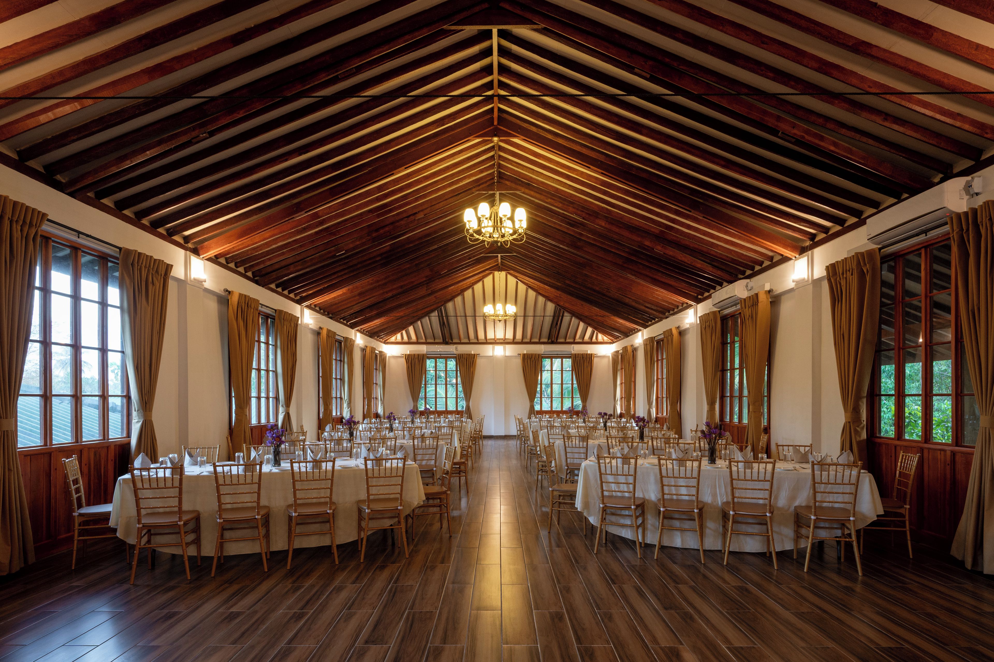 Ein großer Saal mit hohen Decken und Holzbalken, mit Tischen und Stühlen für Speisen eingerichtet.