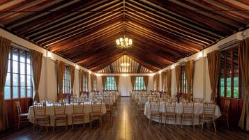 Ein großer Saal mit hohen Decken und Holzbalken, mit Tischen und Stühlen für Speisen eingerichtet.