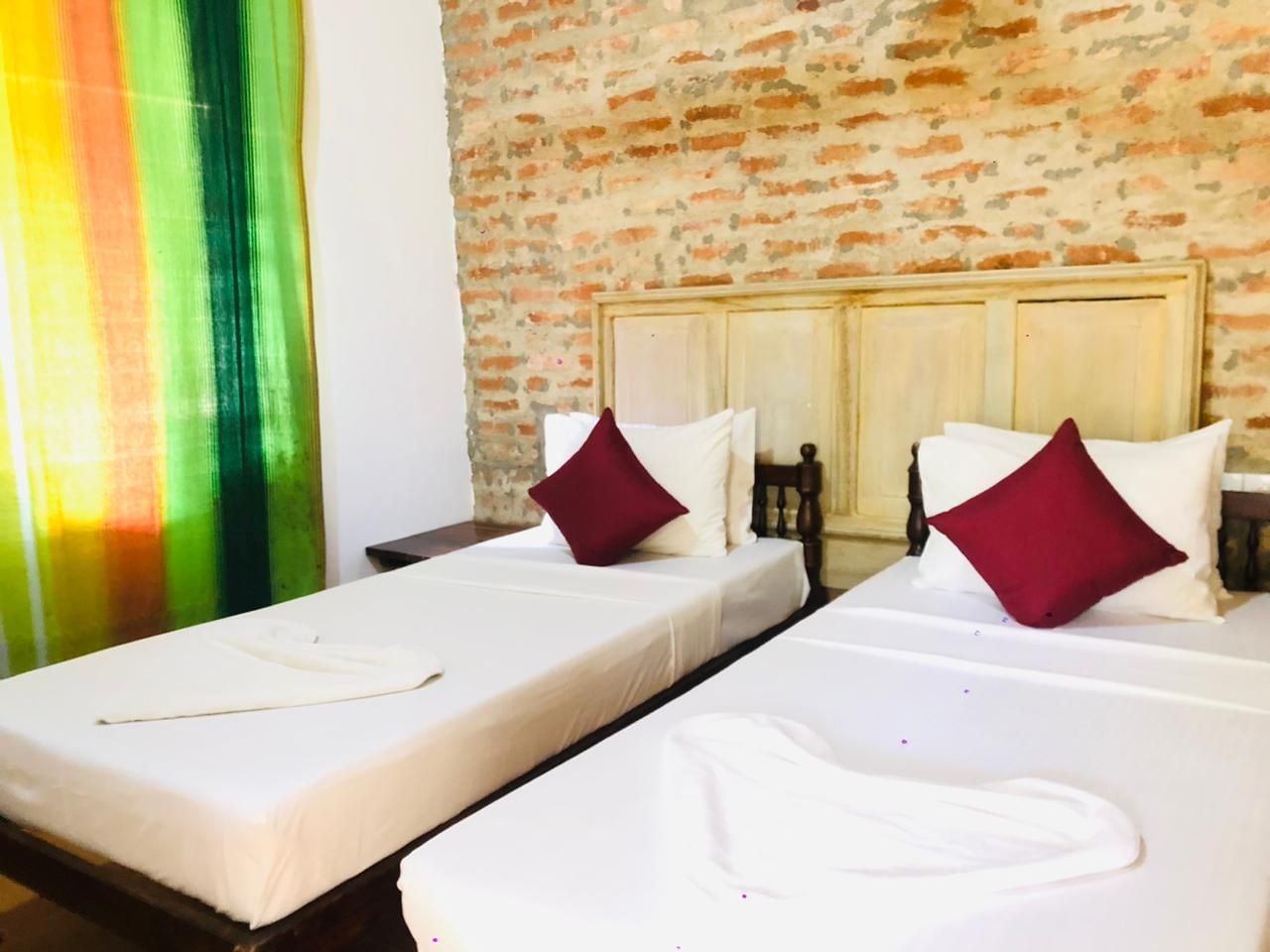 A hotel room with two beds, a brick wall, and a window with a curtain.