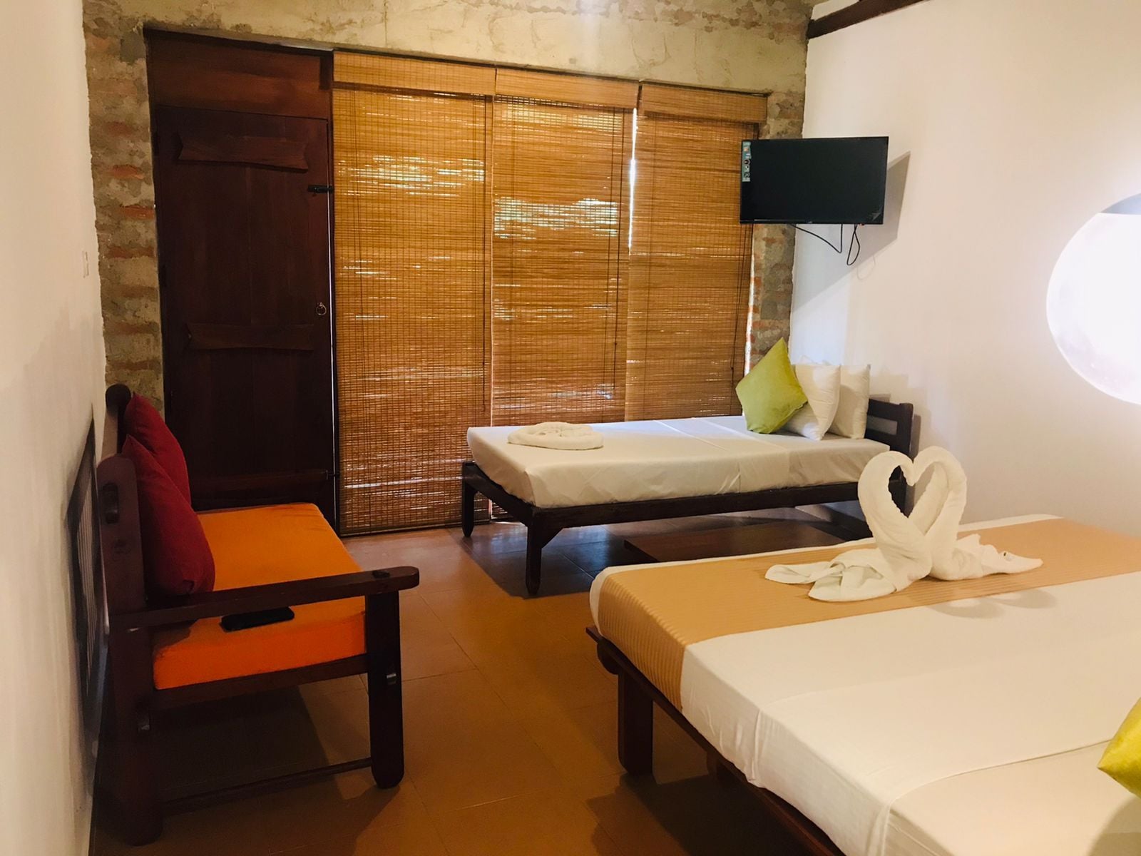 A hotel room with two beds, a television mounted on the wall, and a sliding door with bamboo blinds.