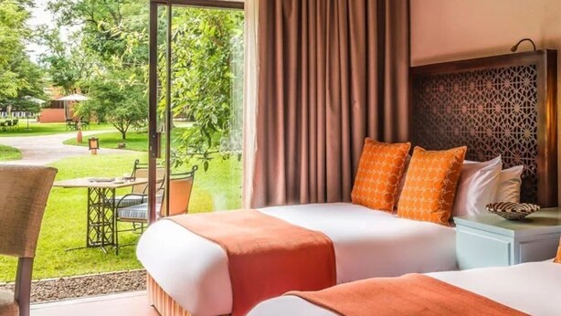 Ein Hotelzimmer mit zwei Betten, Blick auf den Garten und einem Essbereich mit Sitzgelegenheiten im Freien.