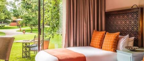 Habitación de hotel con dos camas, vistas al jardín y una zona de comedor con asientos exteriores.