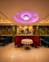Interior de restaurante con una mesa redonda, asientos tapizados en rojo y una pared decorativa con motivos florales.