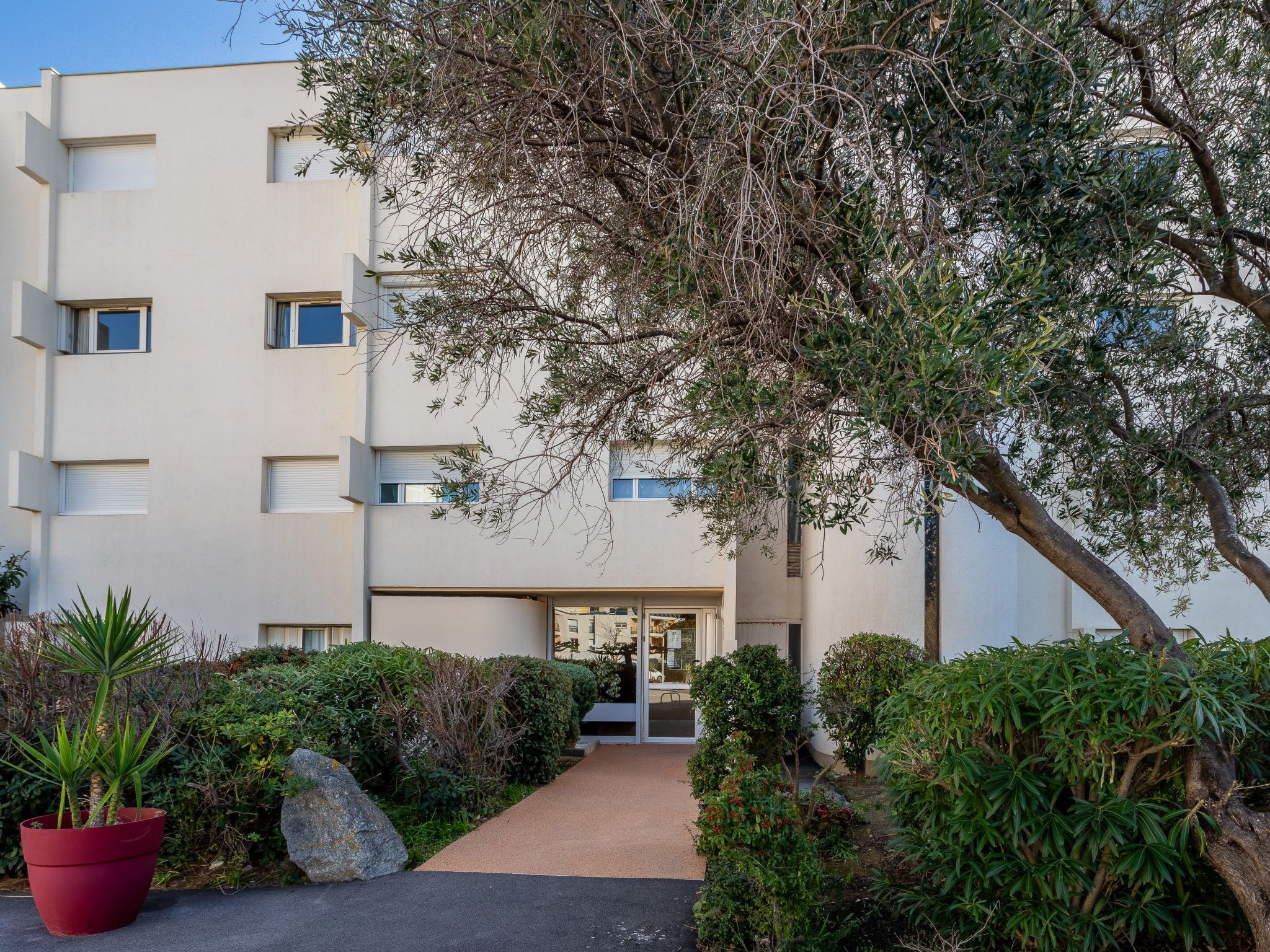 Ein modernes Gebäude mit einem zentralen Eingang, umgeben von Grünflächen und einem Weg zum Eingang.