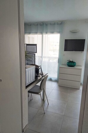 Ein Zimmer mit Schreibtisch, Stuhl, Fernseher und Kommode.