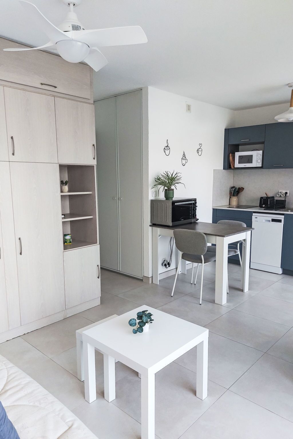 Una cuina moderna amb zona de menjador, armaris blancs i un ventilador de sostre.
