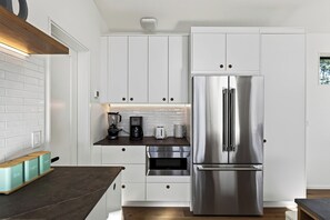 A modern kitchen with white cabinetry, a stainless steel refrigerator, and a coffee maker on the counter.