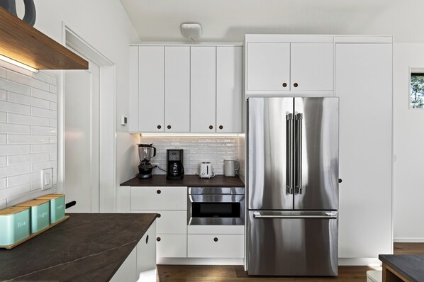 A modern kitchen with white cabinetry, a stainless steel refrigerator, and a coffee maker on the counter.