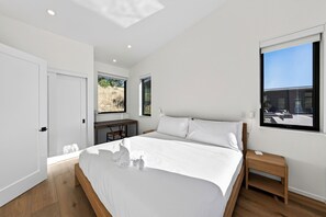 Ein modernes Schlafzimmer mit einem großen Bett, einem Schreibtisch und einem Fenster mit Blick auf ein Gebäude.