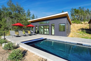 A modern house with a swimming pool, outdoor seating, and a natural landscape.