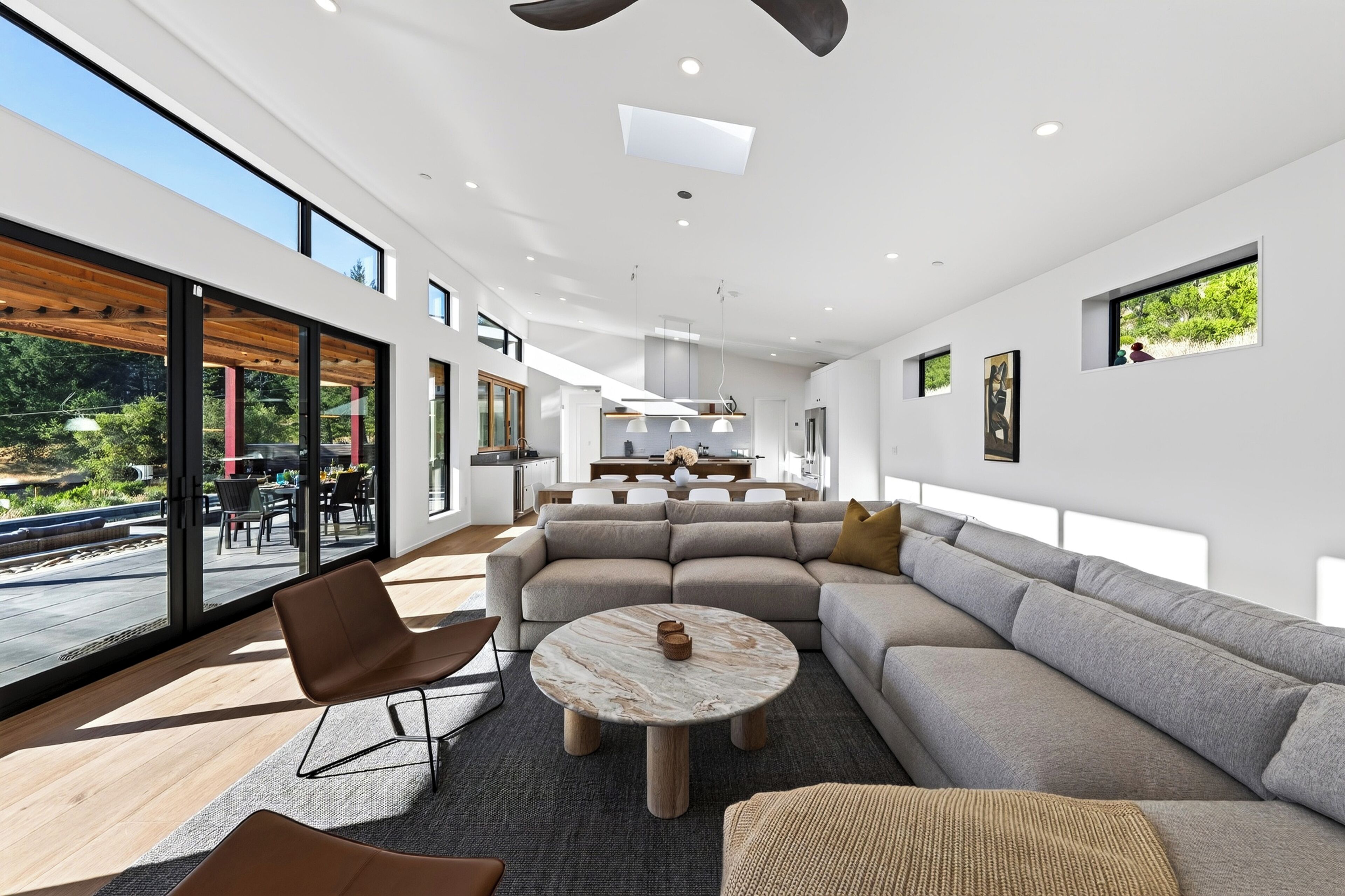 Ein modernes Interieur mit einer großen Eckcouch, einem runden Couchtisch und einem Essbereich mit Blick ins Freie.