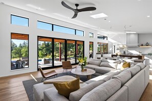 A spacious living area with a large gray sectional sofa, a round coffee table, and a dining area with a kitchen in the background.