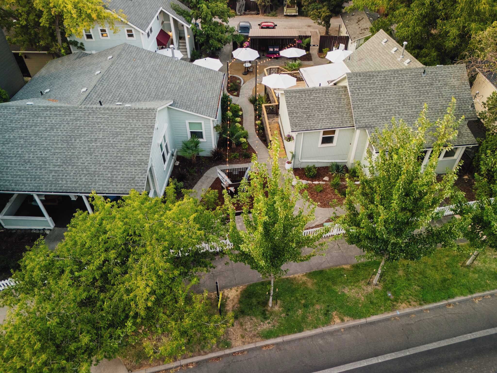 A residential area with multiple houses, a paved driveway, and a small outdoor seating area with umbrellas.